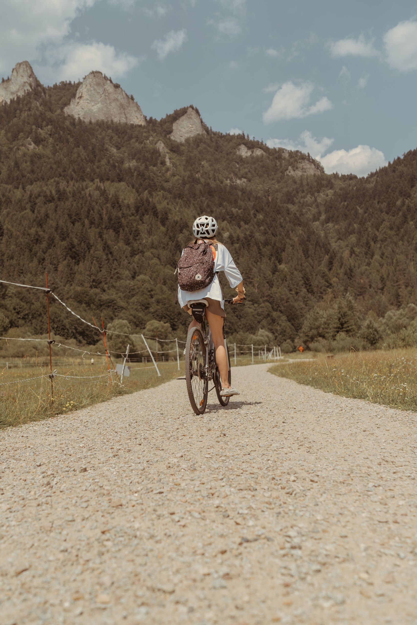 Woman cycling on a dirt road in Sromowce Niżne, Poland, amidst stunning mountain backdrop.